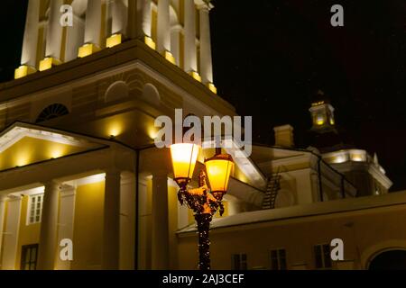 Vintage lampe rue retors avec une guirlande de fête brille dans l'obscurité pendant une chute de neige dans le contexte d'un bâtiment historique Banque D'Images