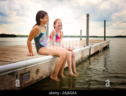 Deux jeunes filles en maillots de bain assis sur un quai à côté du lac rire