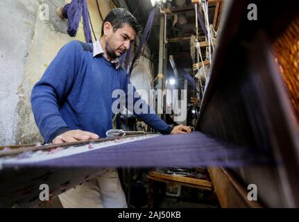 Un travailleur palestinien tisse des tapis sur un métier traditionnel en bois à une fabrique de tapis dans la ville de Gaza.Parler de vieille Gaza, et ce qui s'affiche sont des images d'argile poterie, verrerie colorée, mobilier en bambou et des métiers du bâti ancien tissage de tapis et tapis lumineux. Comme ces professions pourraient être en train de mourir dans le monde entier, le rythme de la baisse est trop rapide à Gaza que sur ses quelque 500 métiers, un seul est encore en activité. Banque D'Images