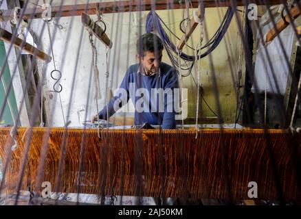 Un travailleur palestinien tisse des tapis sur un métier traditionnel en bois à une fabrique de tapis dans la ville de Gaza.Parler de vieille Gaza, et ce qui s'affiche sont des images d'argile poterie, verrerie colorée, mobilier en bambou et des métiers du bâti ancien tissage de tapis et tapis lumineux. Comme ces professions pourraient être en train de mourir dans le monde entier, le rythme de la baisse est trop rapide à Gaza que sur ses quelque 500 métiers, un seul est encore en activité. Banque D'Images