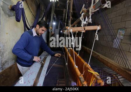 Un travailleur palestinien tisse des tapis sur un métier traditionnel en bois à une fabrique de tapis dans la ville de Gaza.Parler de vieille Gaza, et ce qui s'affiche sont des images d'argile poterie, verrerie colorée, mobilier en bambou et des métiers du bâti ancien tissage de tapis et tapis lumineux. Comme ces professions pourraient être en train de mourir dans le monde entier, le rythme de la baisse est trop rapide à Gaza que sur ses quelque 500 métiers, un seul est encore en activité. Banque D'Images