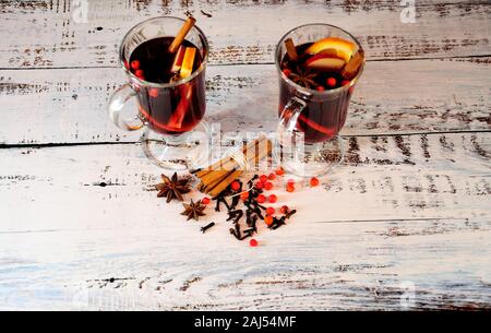 Deux verres de vin chaud avec des tranches de fruits et d'épices se tenir près d'une poignée d'anis étoile, des bâtons de cannelle et de girofle sur une table en bois. Voir bof Banque D'Images