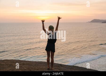 Jeune femme debout sur le rocher à la plage au coucher du soleil Banque D'Images