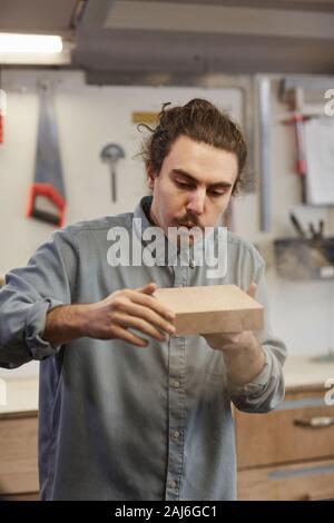 Les jeunes travailleurs manuels avec moustache holding bar en bois et de la sciure de soufflage il tout en travaillant en atelier Banque D'Images
