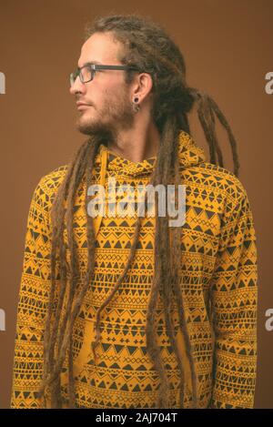 Studio shot of young handsome man avec des dreadlocks wearing hoodie contre fond brun Banque D'Images