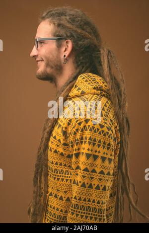 Studio shot of young handsome man avec des dreadlocks wearing hoodie contre fond brun Banque D'Images