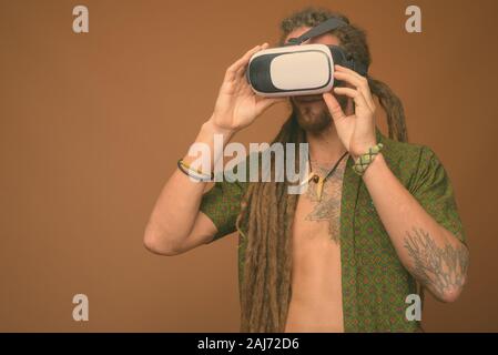 Studio shot of young handsome man avec des dreadlocks portant chemise déboutonnée contre fond brun Banque D'Images