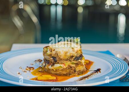 Moussaka grecque un repas à la carte sur plaque blanche à un restaurant en plein air par piscine Banque D'Images