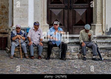 Les hommes âgés à traîner comme des amis assis sur les marches de l'entrée de l'enfant d'un ancien bâtiment à Obidos, Portugal. Photographie : Iris de Reus Banque D'Images