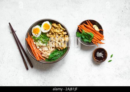 Soupe ramen japonais avec des oeufs, du poulet épicé et verts sur fond blanc. La nourriture asiatique, bol de ramen pour déjeuner sain, copiez l'espace. Banque D'Images