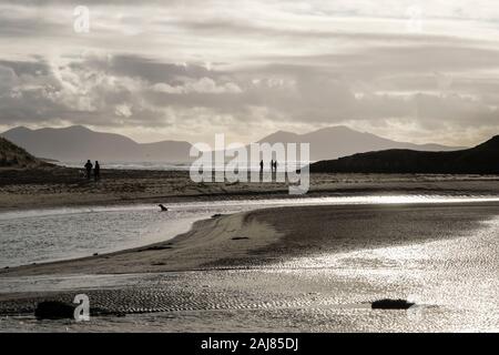 Vue en contre-jour d'Afon Ffraw avec river people walking on Traeth Mawr beach avec des montagnes au-delà en hiver. Aberffraw Isle of Anglesey Pays de Galles UK Banque D'Images