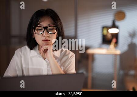 Asian pensive businesswoman wearing eyeglasses à surveiller à son ordinateur portable et de travailler au bureau Banque D'Images