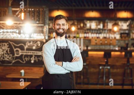 Smiling waiter barman barbu debout sur le fond d'un bar. Banque D'Images