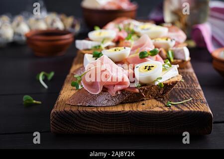 Bruschetta au prosciutto/jamon italienne antipasti. En-cas délicieux avec du pain, fromage brie et oeufs de cailles. Aliments santé, tapas Banque D'Images