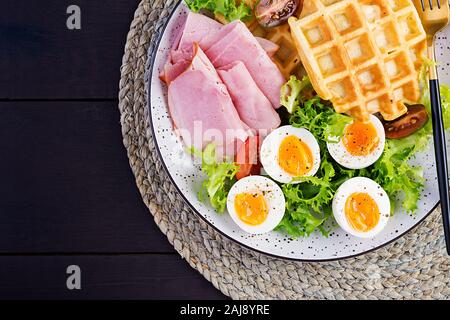 Petit déjeuner avec des gaufres de semoule, oeuf dur, jambon et tomate sur fond sombre. Apéritifs, brunch, en-cas. Alimentation saine. Vue de dessus, les frais généraux, les savs copie Banque D'Images