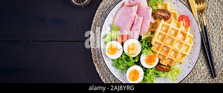 Petit déjeuner avec des gaufres de semoule, oeuf dur, jambon et tomate sur fond sombre. Apéritifs, brunch, en-cas. Alimentation saine. Vue de dessus, les frais généraux, la bannière Banque D'Images