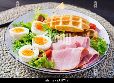 Petit déjeuner avec des gaufres de semoule, oeuf dur, jambon et tomate sur fond sombre. Apéritifs, brunch, en-cas. Alimentation saine. Banque D'Images