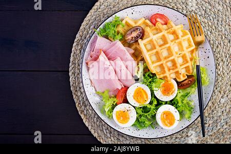 Petit déjeuner avec des gaufres de semoule, oeuf dur, jambon et tomate sur fond sombre. Apéritifs, brunch, en-cas. Alimentation saine. Vue de dessus, les frais généraux, les savs copie Banque D'Images