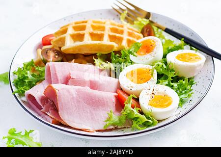 Petit déjeuner avec des gaufres de semoule, oeuf dur, jambon et tomate sur fond blanc. Apéritifs, brunch, en-cas. Alimentation saine. Banque D'Images