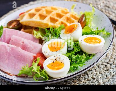 Petit déjeuner avec des gaufres de semoule, oeuf dur, jambon et tomate sur fond sombre. Apéritifs, brunch, en-cas. Alimentation saine. Banque D'Images