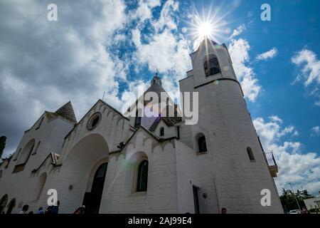 ALBEROBELLO, ITALIE - 28 août 2018 - Ville de Alberobello Trulli blanchis à la tuile de toit en pierre de cône de maisons dans les Pouilles est visité chaque année par des millions de touristes. L'église avec la diffraction de la lumière du soleil Banque D'Images