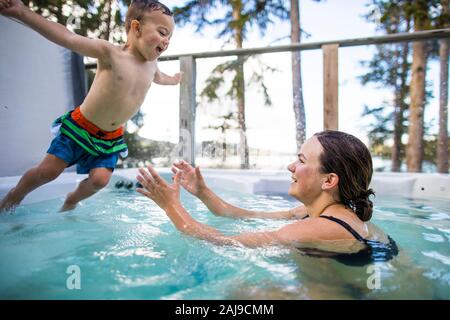 Jeune garçon sautant dans la piscine, maman attendant de l'attraper. Banque D'Images