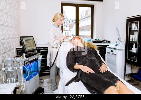 Femme médecin faisant led rouge luminothérapie pour jeune femme dans la clinique de beauté, soins du visage pour la thérapie photo peau. Anti-âge, photo-rajeunissement pro Banque D'Images