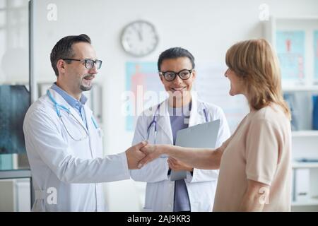 Mâle mature doctor shaking hands à woman nurse standing près de par eux et qu'ils coopèrent à la clinique smiling Banque D'Images