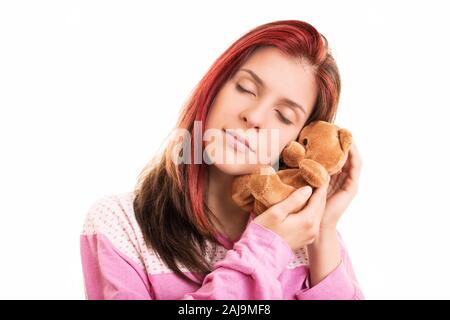 Gros plan d'une belle jeune fille en pyjama rose serrant une peluche ours en peluche brun, isolé sur un fond blanc. Banque D'Images