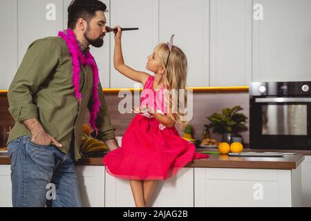 Petite fille mignonne appliquant de la poudre cosmétique sur le nez du père Banque D'Images