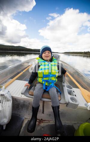 Jeune garçon assis dans un bateau en aluminium pendant la pêche. Banque D'Images