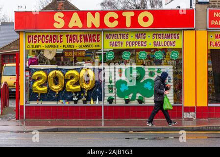 Sancto partie shop à Southend, Essex, UK avec 2020 ballons dans fenêtre. Nouvelle Année. Nouvelle décennie. Un mâle, un homme, en passant par la concentration sur téléphone mobile. La pluie Banque D'Images