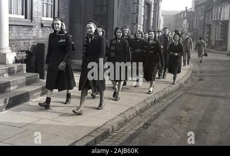 Années 1950, des écolières et des écoliers historiques et uniformés dans leurs manteaux et fendeurs d'école marchant le long d'une rue secondaire anglaise sur leur chemin vers un service d'église, Angleterre, Royaume-Uni. Banque D'Images