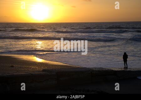 Seule femme regardant le soleil se coucher sur la mer sur la côte galloise. Banque D'Images