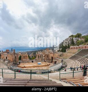 Catane, Italie - 02 octobre 2017 : ruines de l'ancien théâtre grec de Taormina, Sicile avec la queue de fumée sur l'Etna s'étendant sur la Giardini Banque D'Images