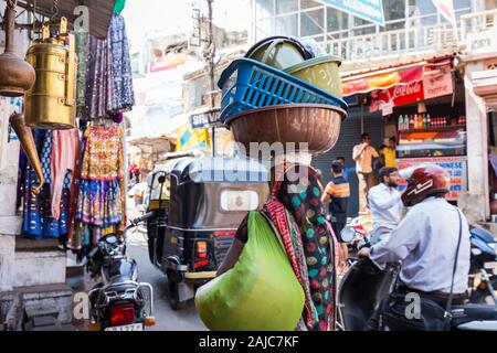 Udaipur, Inde - 04 mars 2017 : les choses sur sa tête : Bassins pour laver les vêtements. Elle marche le long d'une rue étroite entre petite épicerie s Banque D'Images