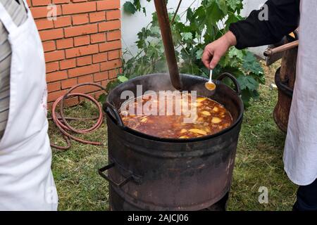La cuisson du ragoût traditionnel dans un grand chaudron d'extérieur en métal. Dégustation de qualité avec une cuillère par l'un des cuisiniers les concurrents. Banque D'Images