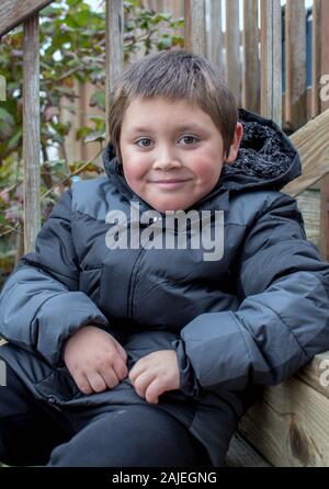 Un jeune garçon en manteau chaud pose sur le bois pas de son accueil Banque D'Images