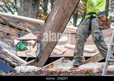 Un travailleur supprime rotten feuilles de bois d'une vieille maison, de sorte qu'il peut être remplacé par le bois frais et de nouveaux bardeaux Banque D'Images