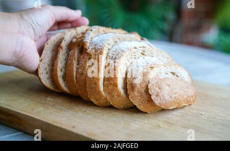 Main tenant une miche de pain au levain tranché sur planche de bois Banque D'Images