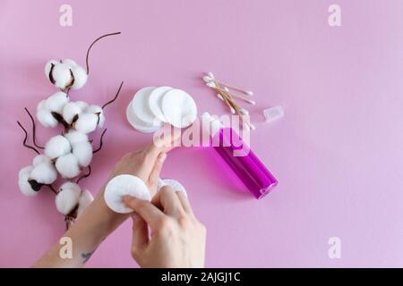 Pour la dépose de coton femme maquillage avec les mains et les cosmétiques sur fond rose mise à plat. Direction générale de fleurs séchées de coton. Banque D'Images