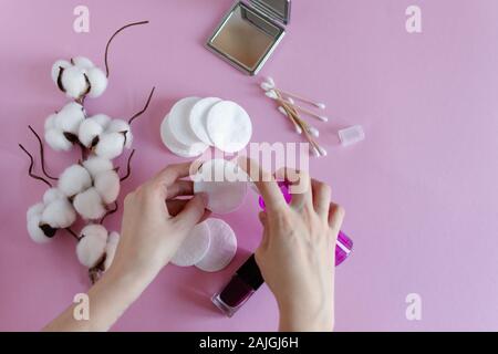 Pour la dépose de coton femme maquillage avec les mains et les cosmétiques sur fond rose mise à plat. Direction générale de fleurs séchées de coton. Banque D'Images