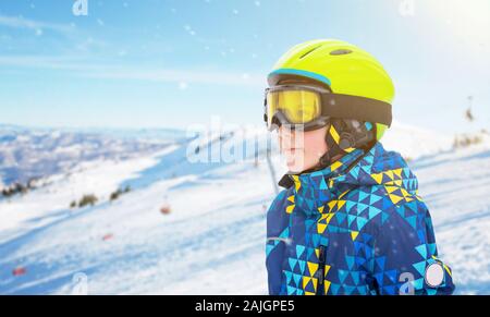 Garçon avec casque de ski, lunettes vert jaune et bleu au centre de ski. Pistes de ski et en arrière-plan. À côté de l'espace de copie Banque D'Images