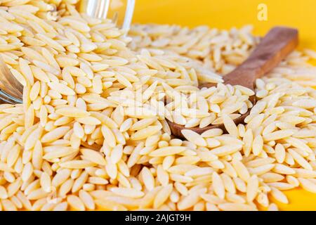 Grains de nouilles d'orge avec cuillère en bois sur fond jaune. Banque D'Images