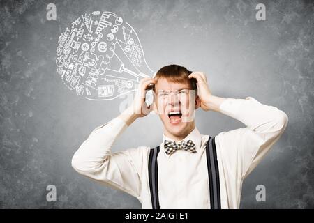 Redhead student stress garde les mains sur la tête. Jeune homme dans la panique sur fond de mur gris avec idée lightbulb esquisse les frais généraux. Gros problème Banque D'Images