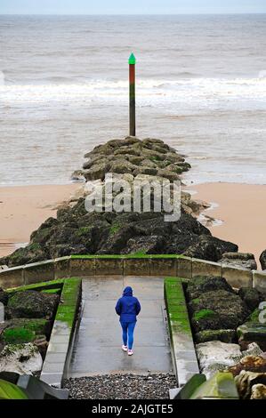 Personne en bleu en marchant le long du pont en béton, d'un brise-lames par l'homme sur la plage,Rossall Fleetwood Banque D'Images