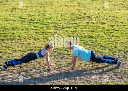 Jeune couple de mettre en place les sportifs boy and girl doing exercise sur l'herbe verte de l'extérieur du stade. Banque D'Images