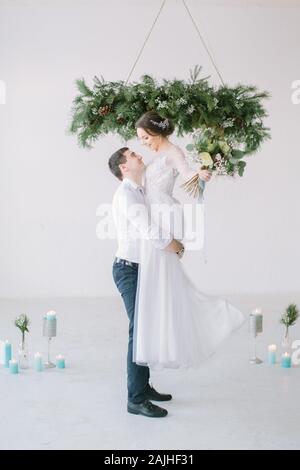 Le marié a levé la mariée dans ses bras. L'épouse dans le luxe robe de mariée blanche dans les bras de l'époux de rire. Cérémonie de mariage blanc lumière Banque D'Images