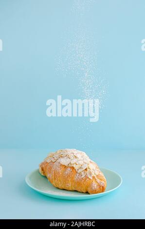 La chute du sucre en poudre sur des croissants adossés sur fond bleu. L'espace de copie, à la verticale. Banque D'Images
