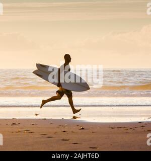 Surfeur sur la plage en cours d'exécution avec surfbard est prêt à naviguer Banque D'Images